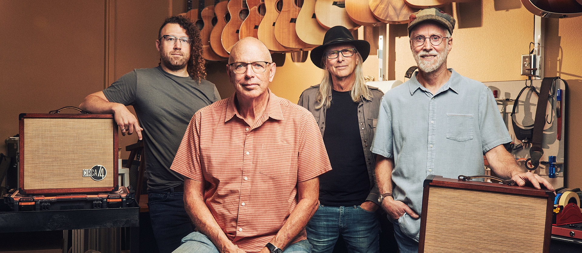 Image with 4 men sitting and standing in a workshop looking at the camera